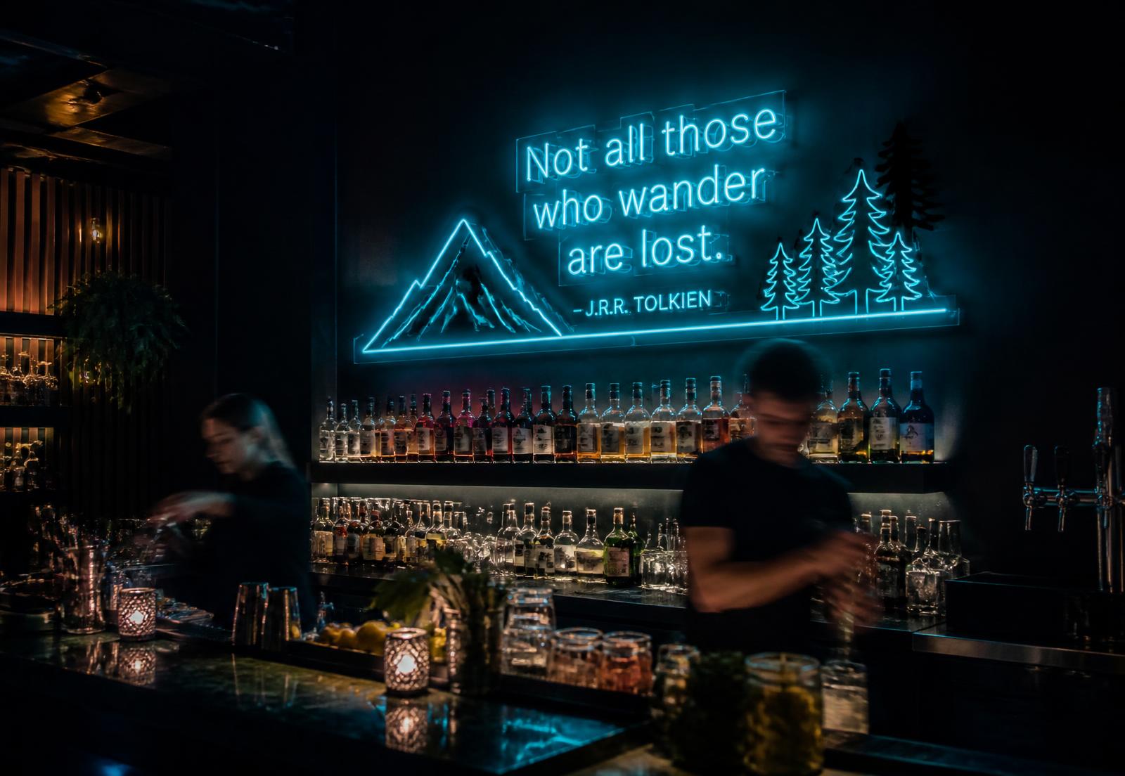 Cyan LED neon sign glowing above the back bar of a dark cocktail lounge